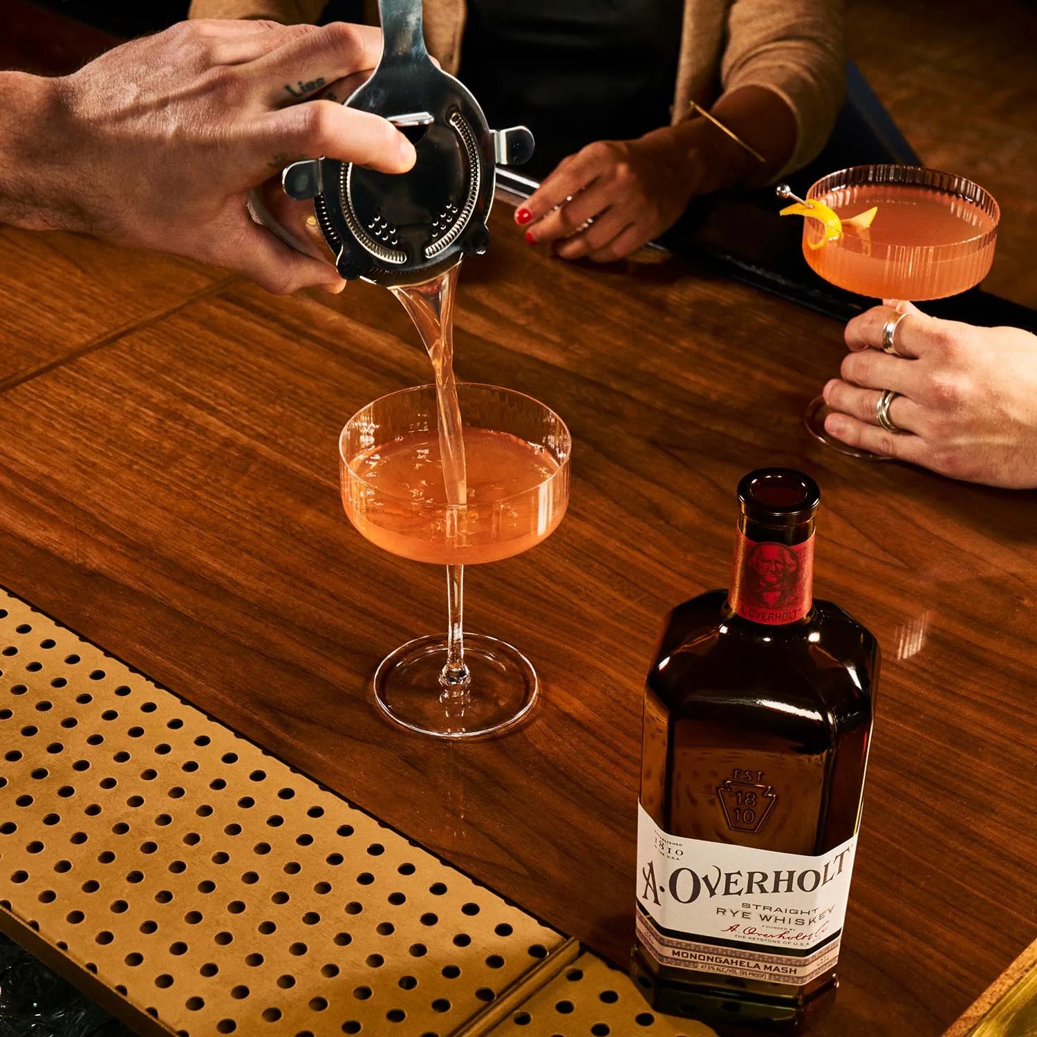 Scofflaw cocktail being strained into a glass, with Monongahela Mash Straight Rye American Whisky Old Overholt.