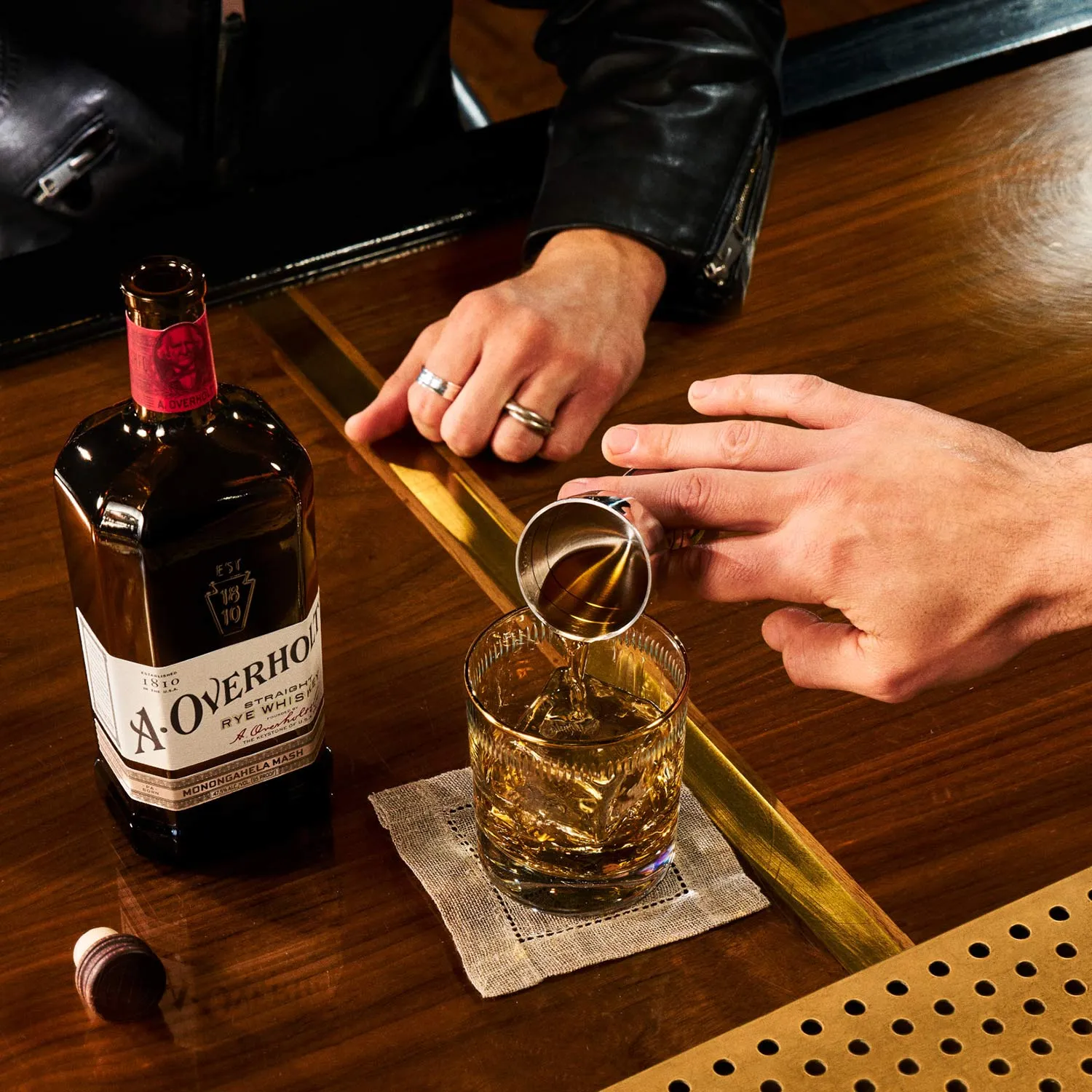 Whiskey Neat being poured into a glass, next to Monongahela Mash Straight Rye American Whisky Old Overholt.