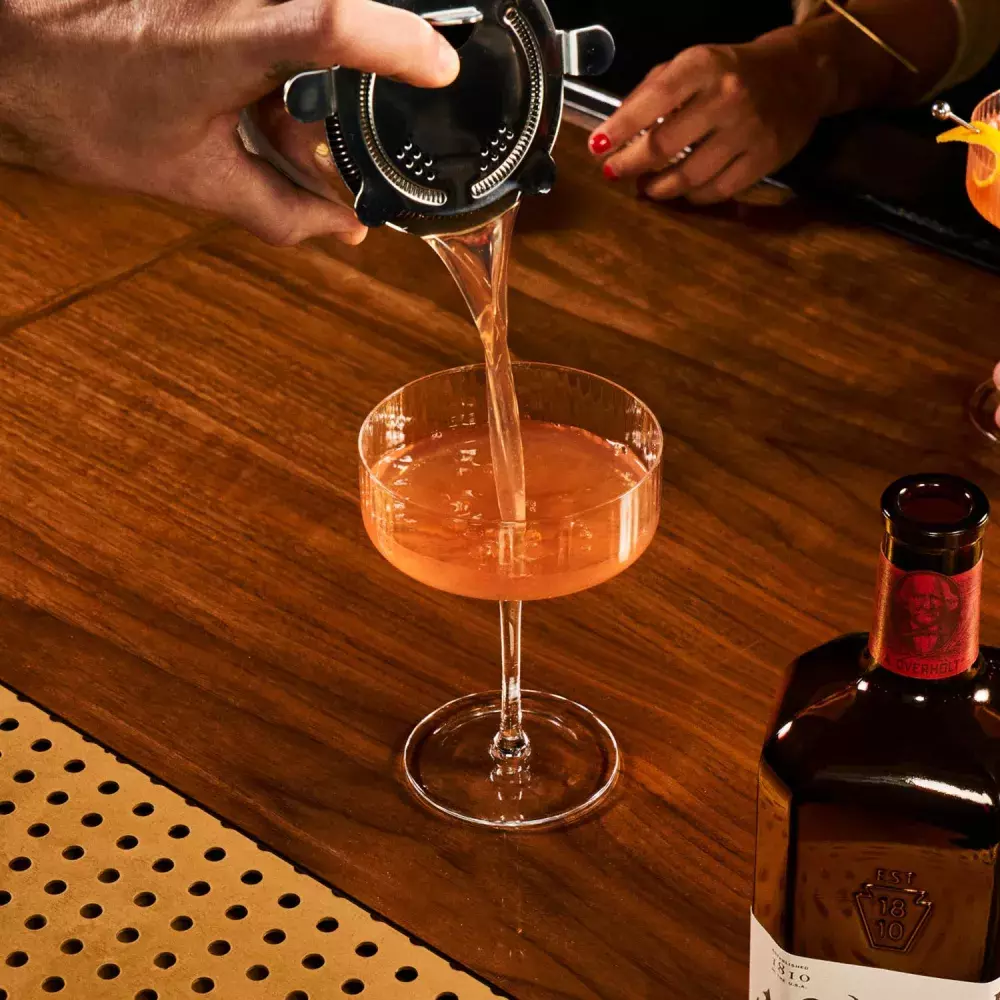 Scofflaw cocktail being strained into a glass, with Monongahela Mash Straight Rye American Whisky Old Overholt.