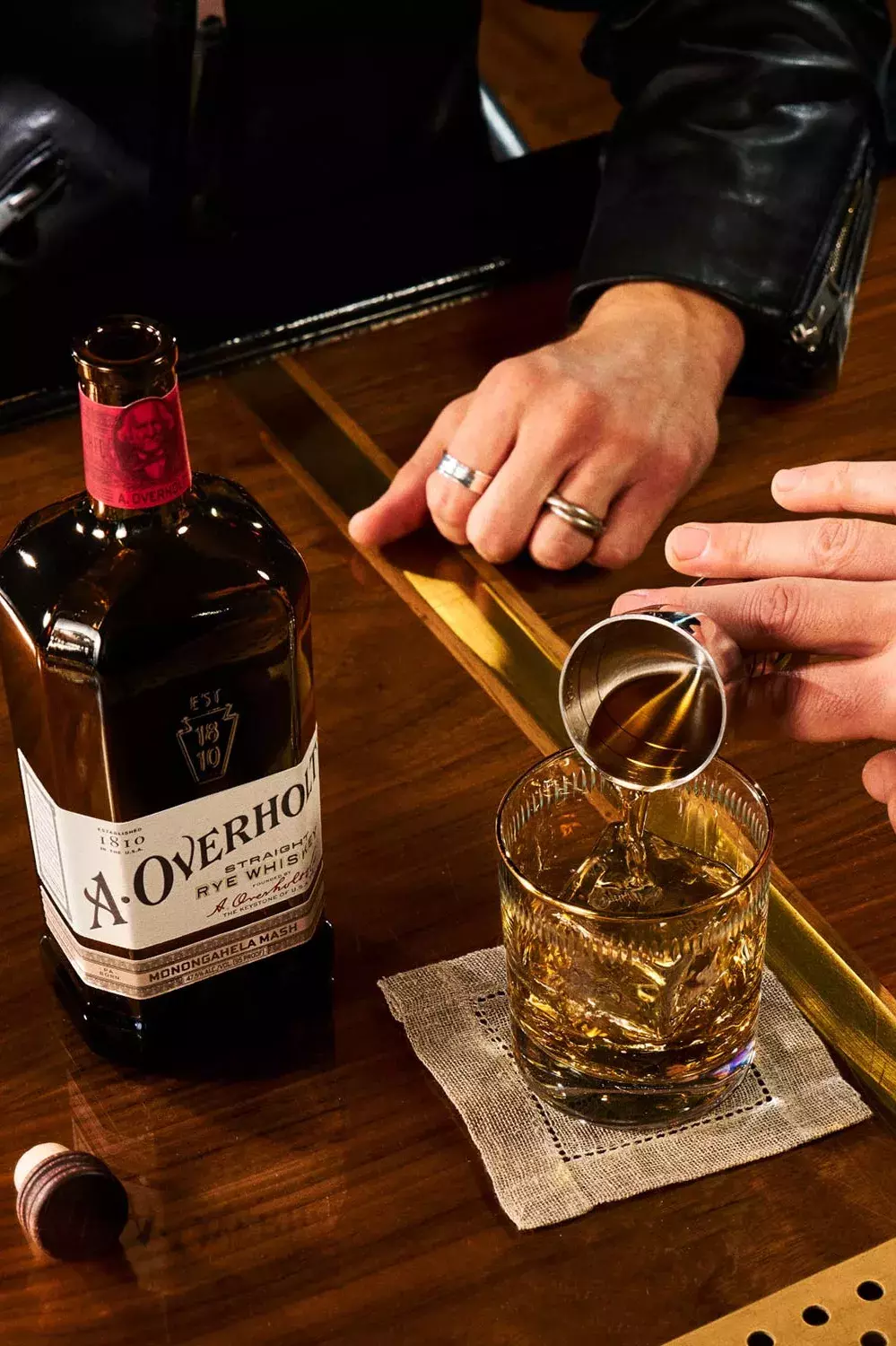Whiskey Neat being poured into a glass, next to Monongahela Mash Straight Rye American Whisky Old Overholt.