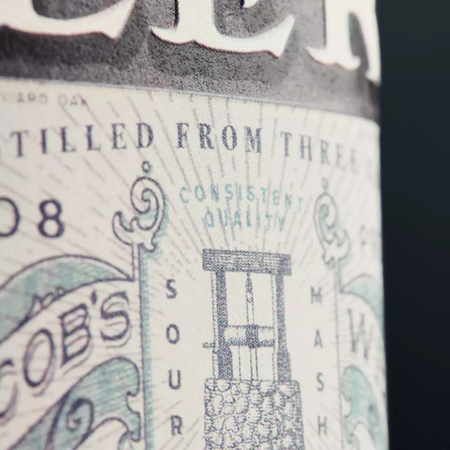 A close-up of a whiskey bottle label, showing the fine print and an etched illustration of a stone water well on the Jacob's Well expression Whisky Hardin's Creek