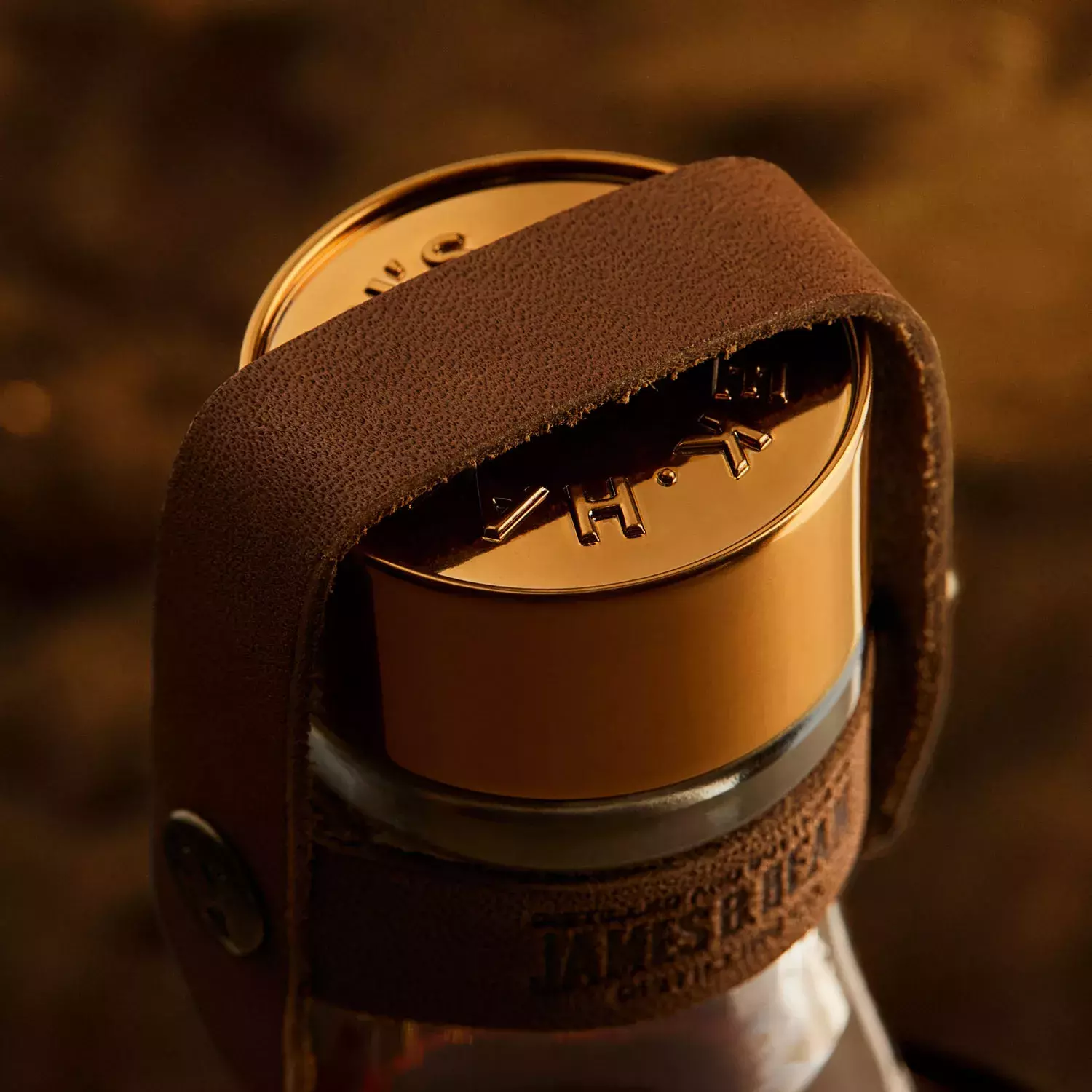 A macro shot of the top of a whiskey bottle, focusing on the golden metal cap with embossed lettering and a brown leather strap wrapped around it Whisky Hardin's Creek.