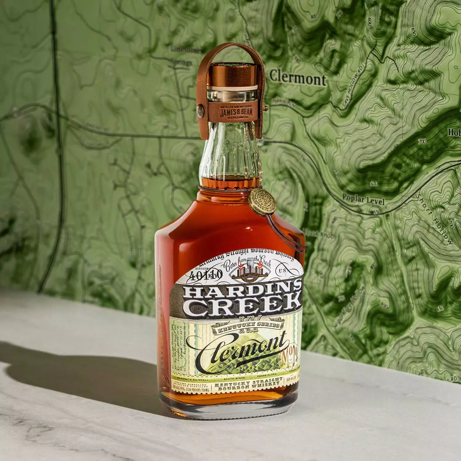 A bottle from the Kentucky Series labeled Clermont, positioned in front of a green and white topographical map featuring the city's name Whisky Hardin's Creek