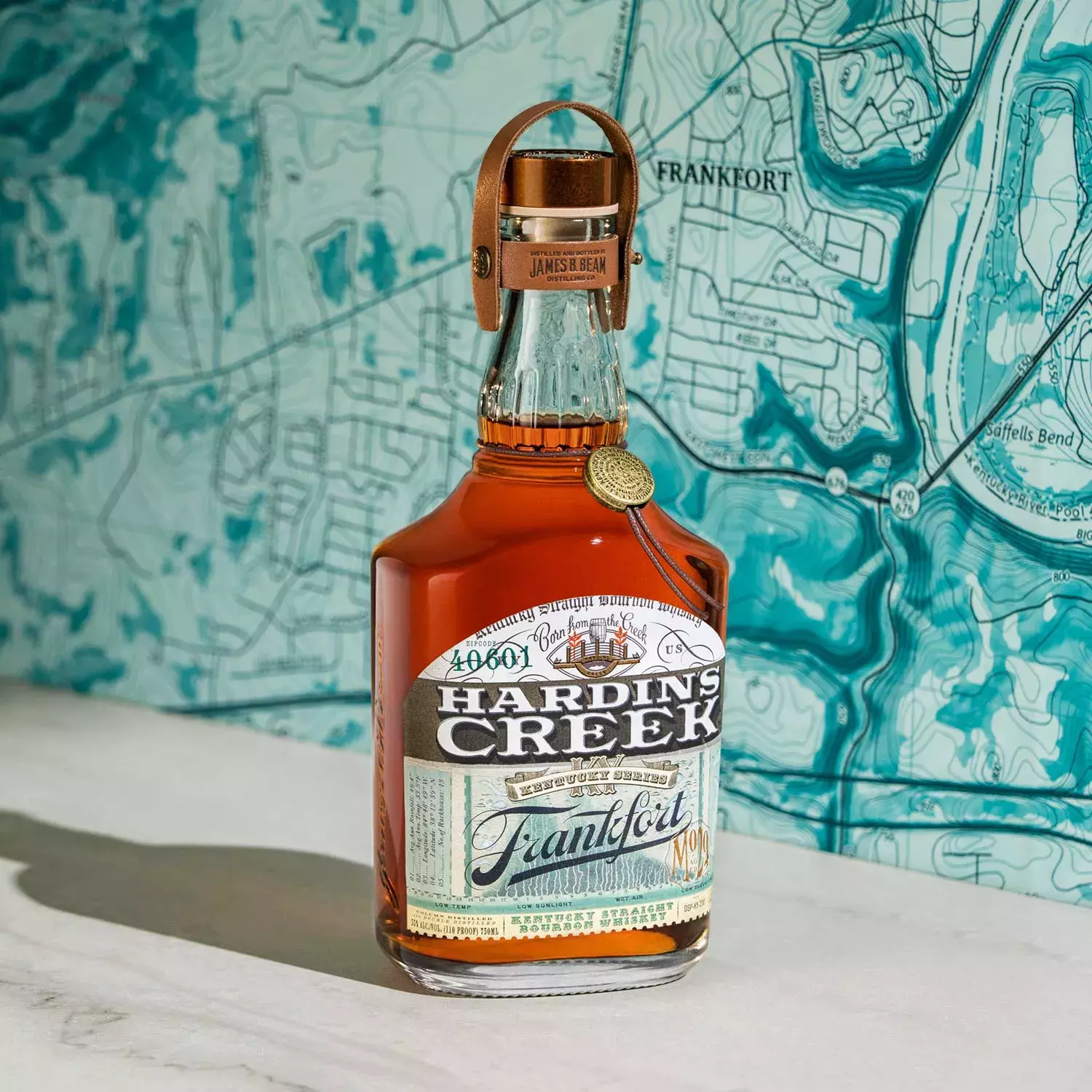A bottle from the Kentucky Series labeled Frankfort, positioned in front of a blue and white topographical map featuring the city's name Whisky Hardin's Creek