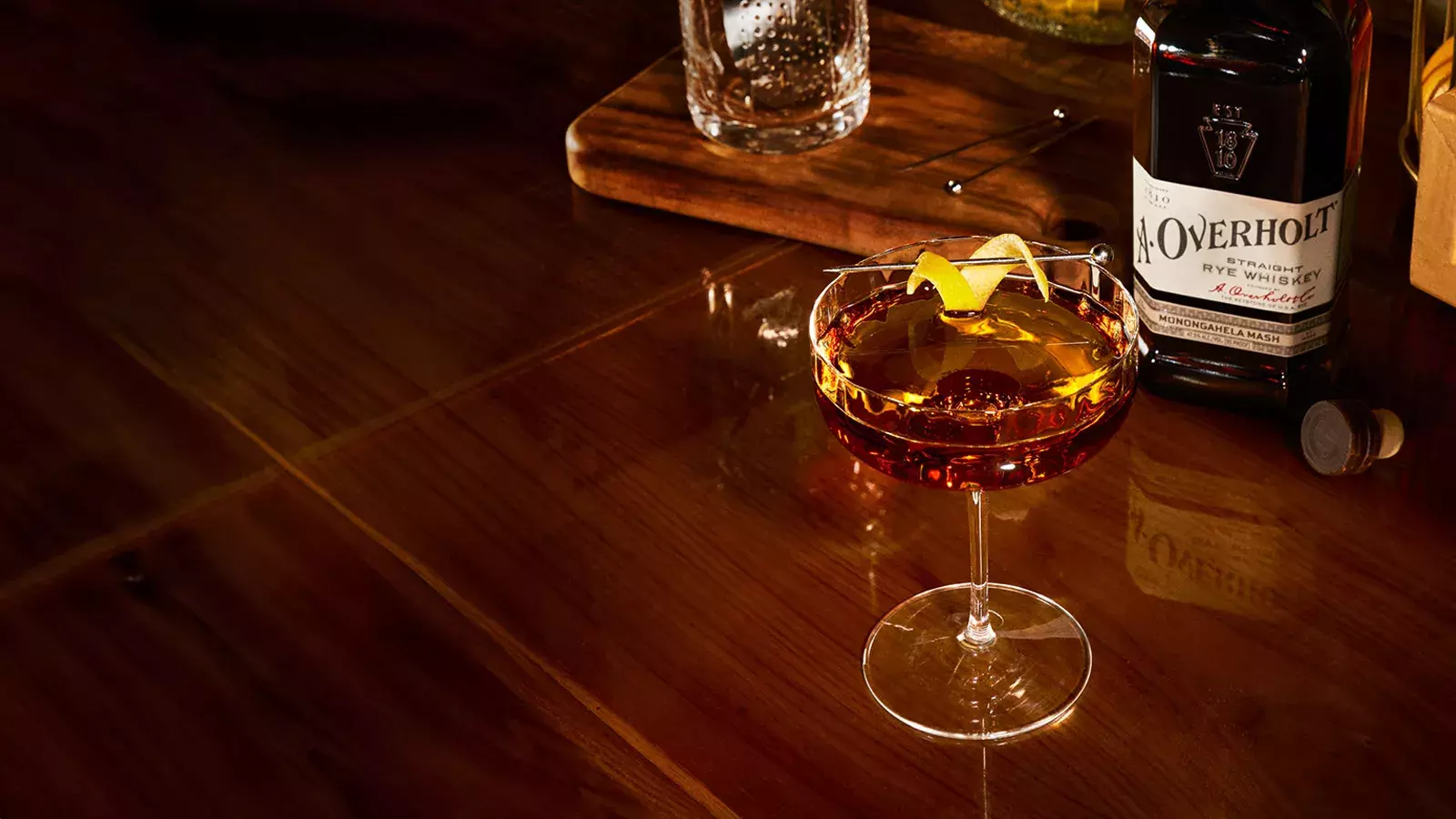 Perfect Manhattan cocktail with a lemon twist, next to Monongahela Mash Straight Rye American Whisky Old Overholt.