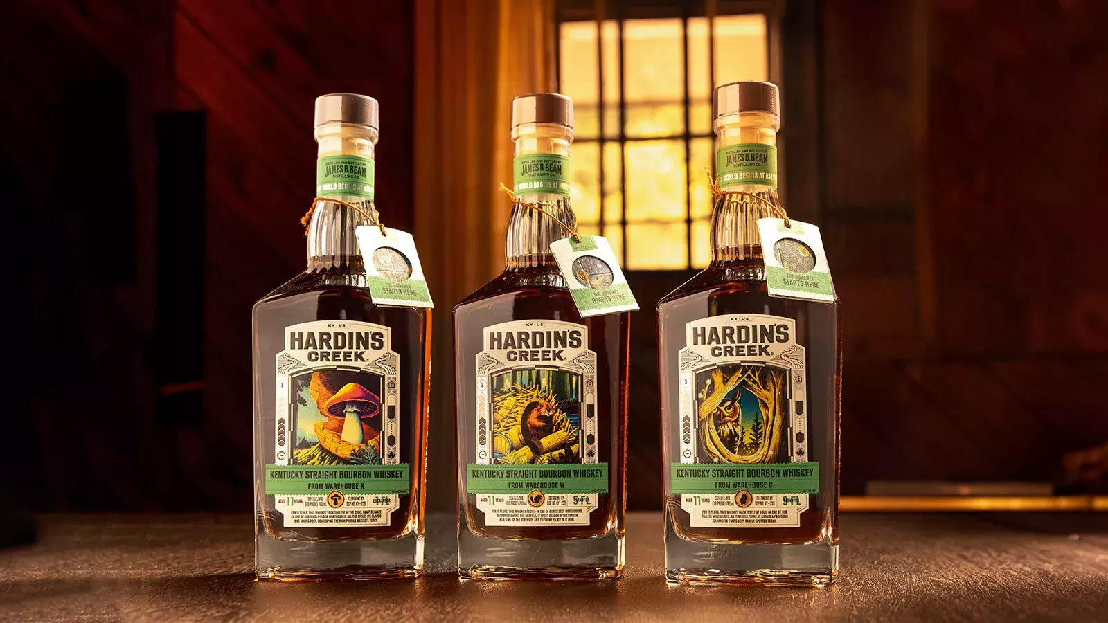 Three square-shouldered bottles (The Mushroom, The Beaver, and The Owl) of the Hardin's Creek Warehouse Series standing on a wooden surface in front of a window Whisky Hardin's Creek