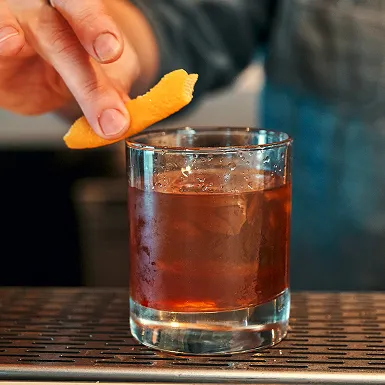 Bartender garnishes a bourbon cocktail with an orange peel in a rocks glass at The Kitchen Table.