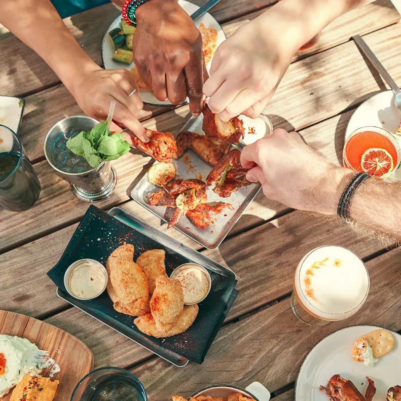Hands reaching for chicken wings at an outdoor gathering at The Kitchen Table restaurant. 