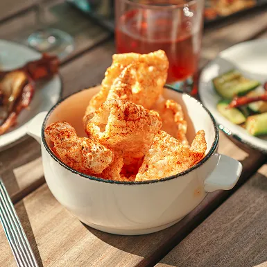 Close-up of a bowl of spiced pork rinds on an outdoor table at The Kitchen Table restaurant.