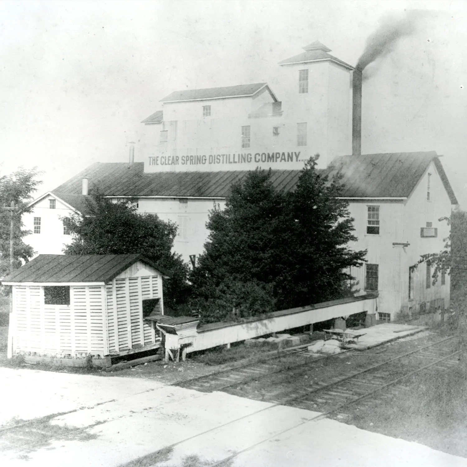 Historic view of the Clear Spring Distilling Company, featuring the iconic smokestack and surrounding buildings.