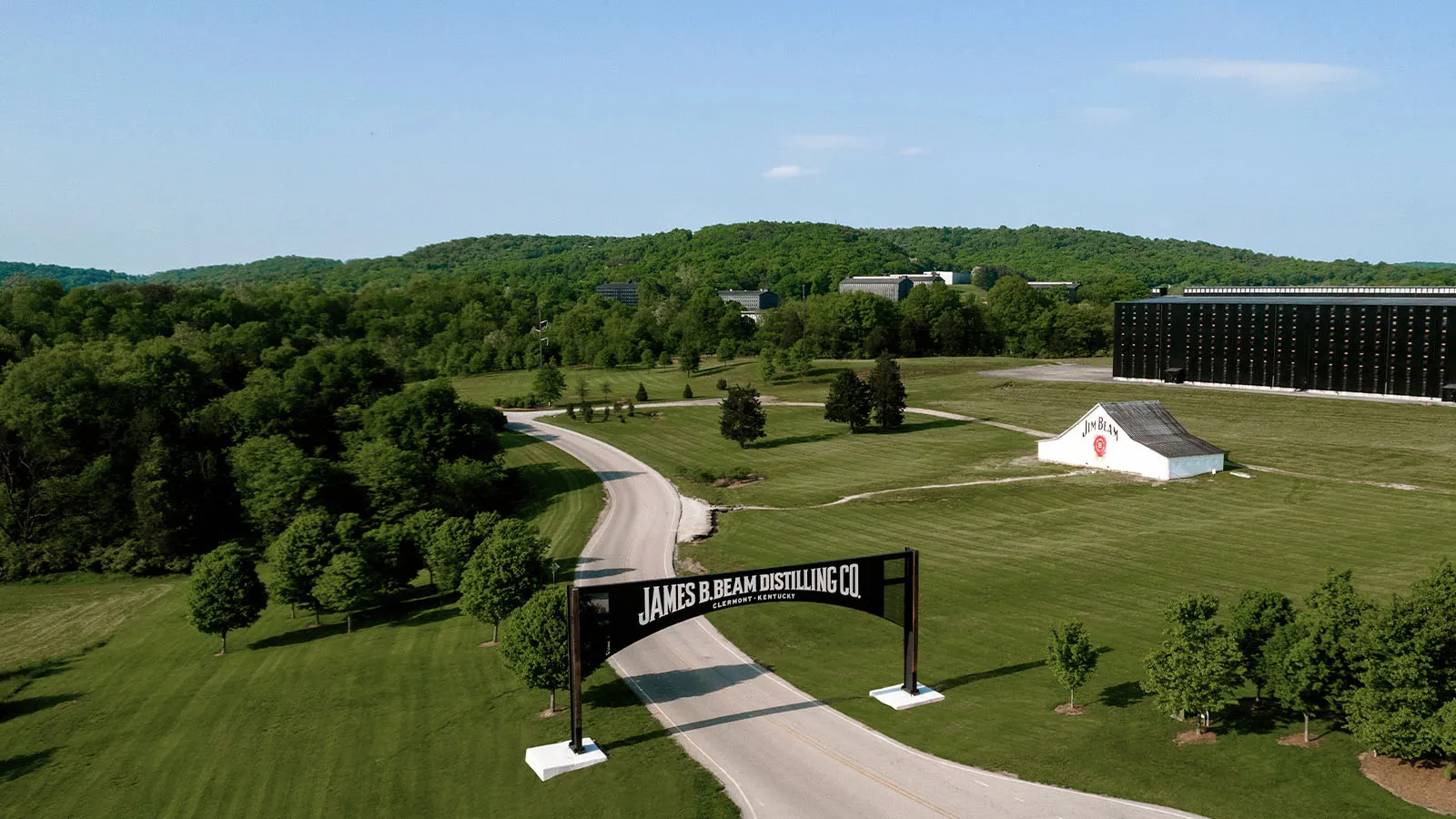 Entrance sign for James B. Beam Distilling Co. in Clermont, KY, with rickhouses and Jim Beam barn visible