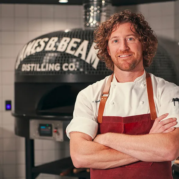 Chef at The Kitchen Table restaurant in front of the James B. Beam wood-fired pizza oven.  Development