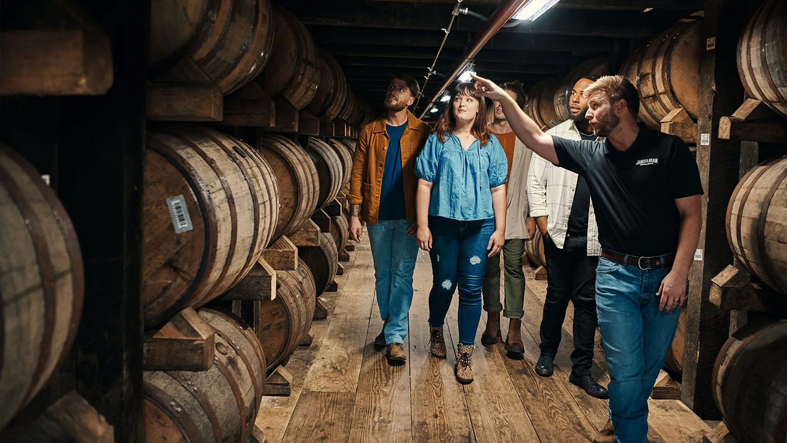 Tour guide guiding a small group tour through a rickhouse, surrounded by aging James B Beam Distilling Co. bourbon barrels.