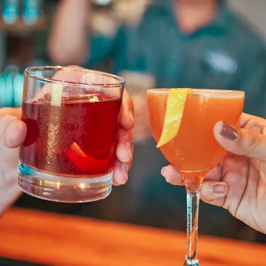 Close-up of two people cheersing with bourbon cocktails at The Kitchen Table bar.  ALT TEXT