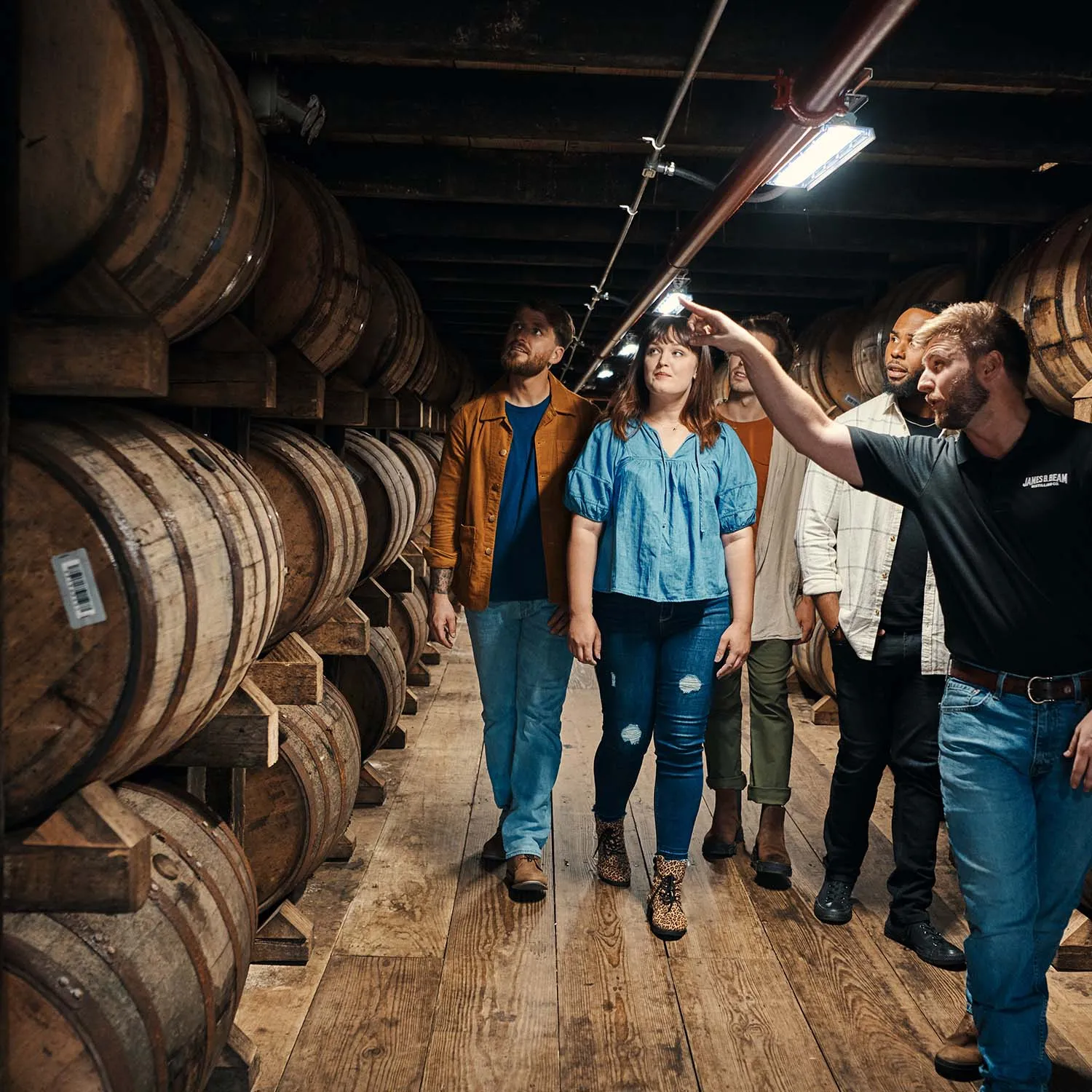 Tour guide pointing inside a James B. Beam rackhouse, showing guests rows of aging bourbon barrels.