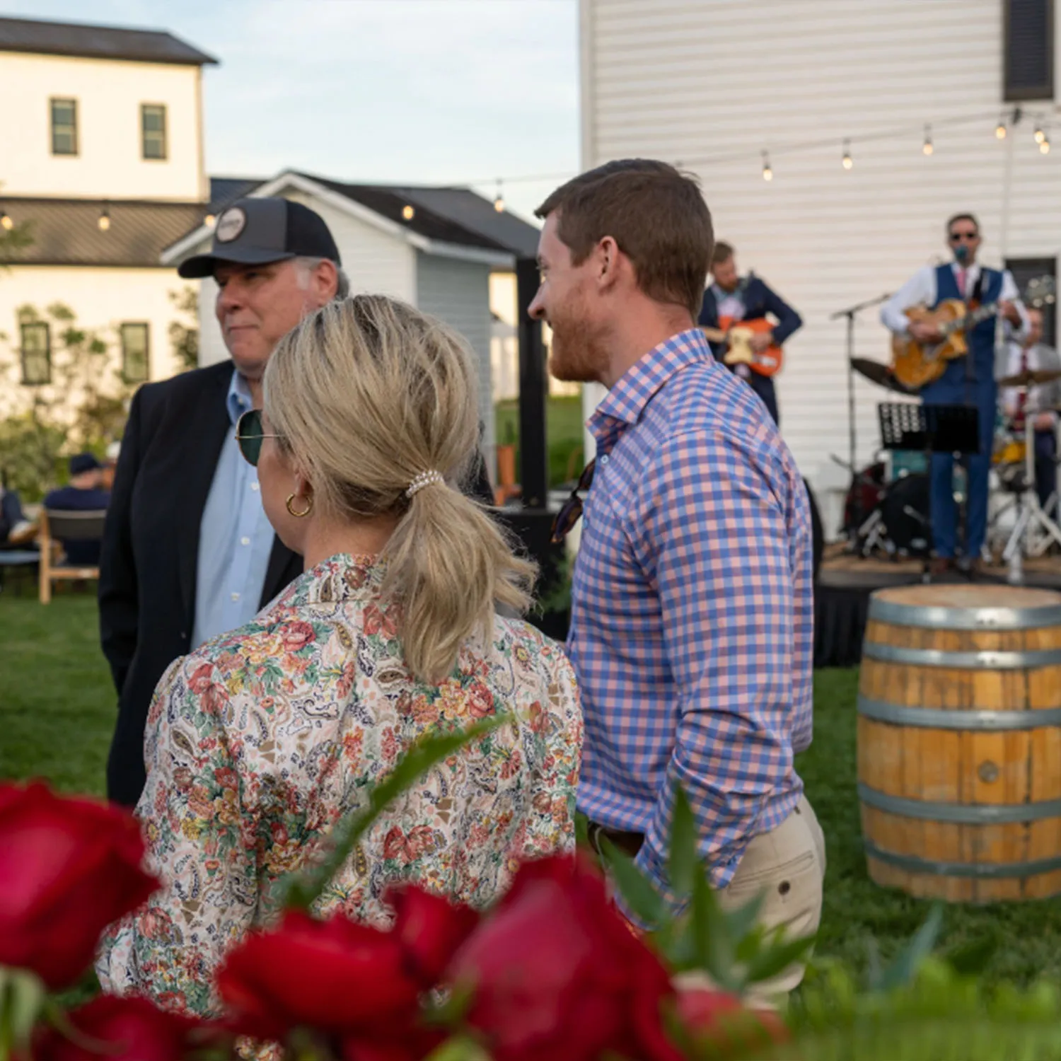 Guests socializing near a bourbon barrel table with a live band performing on the Jim Beam event lawn.