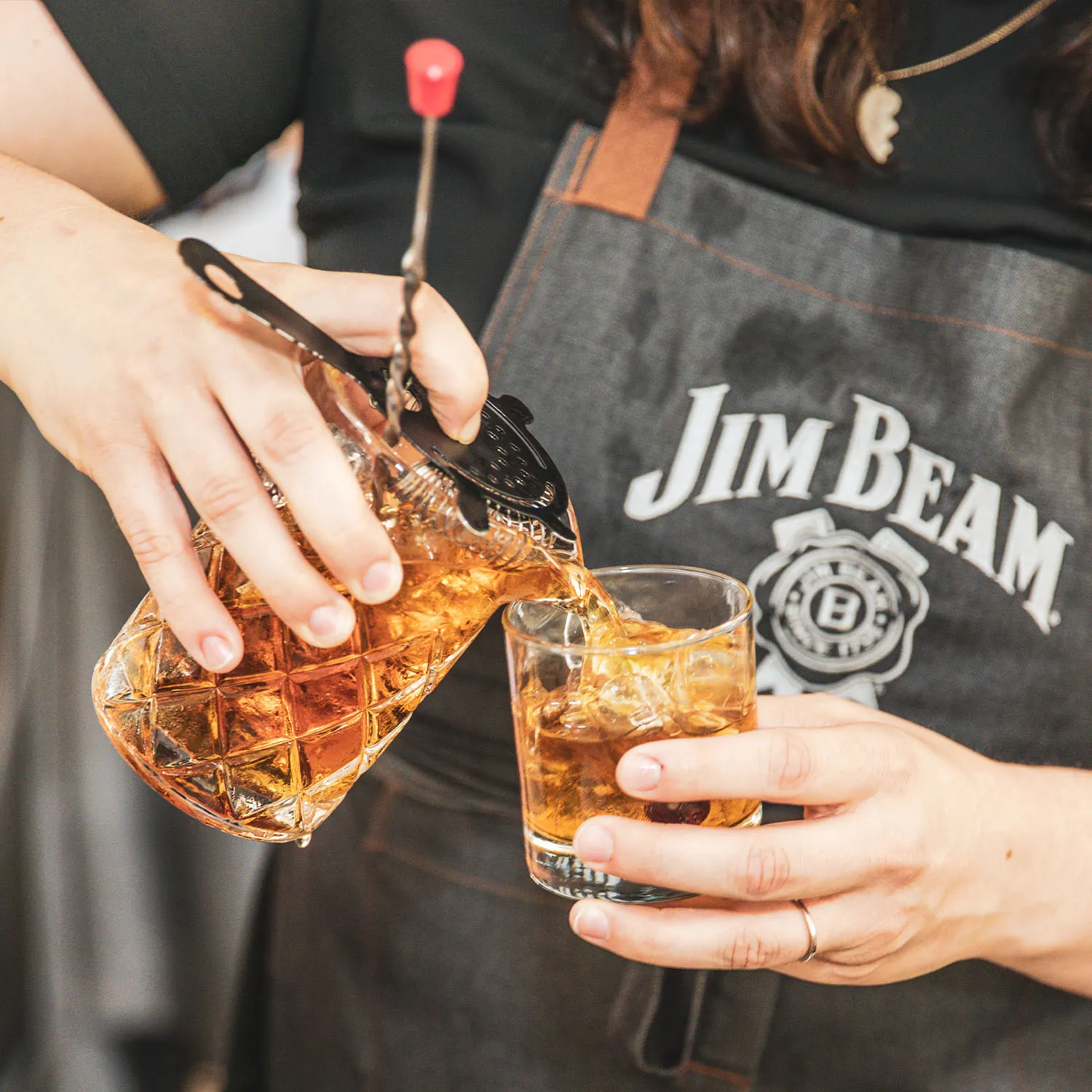 Bartender straining and pouring a Jim Beam bourbon cocktail into a glass with ice.  Development
