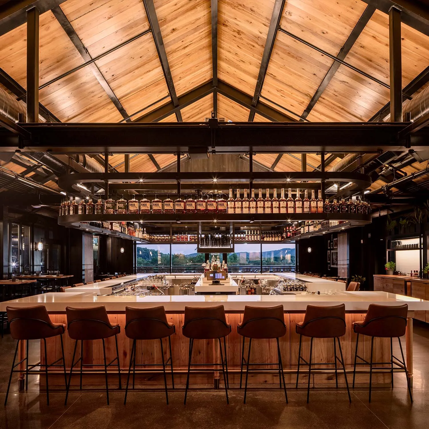 Interior of The Kitchen Table Restaurant with a long bar, rustic wood ceiling, and bourbon display.