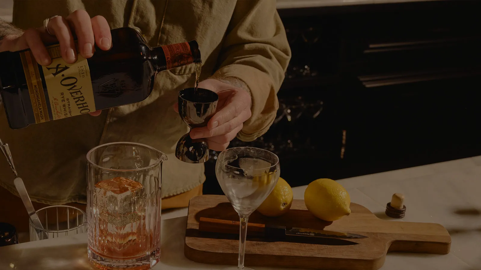 Hand pouring bottle into a glass, with a matchbook on a gold surface, American Whisky Old Overholt.